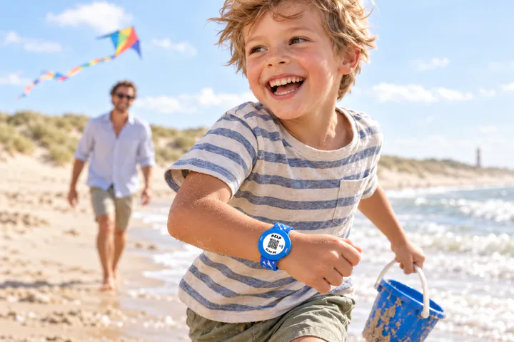 Lachende jongen op het strand met een blauwe ICESCAN-kinderarmband om zijn pols